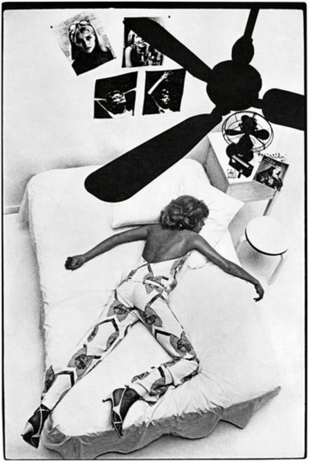 Модель лежит на кровати по диагонали в ярком комбинезоне и белых босоножках с перемычками.