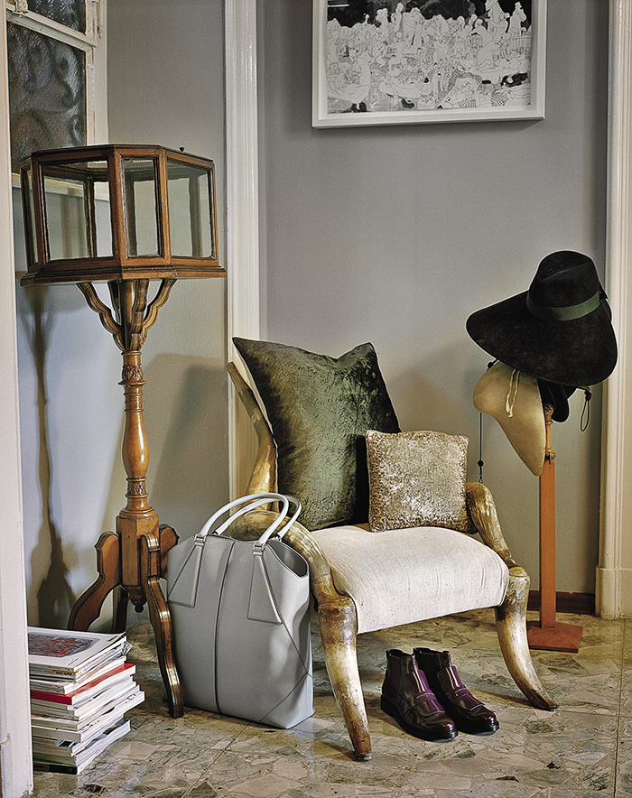 Кожаная сумка, ботинки и шерстяная шляпа, все – из коллекции Tod’s, на фоне антикварной витрины и американского кресла с роговым каркасом